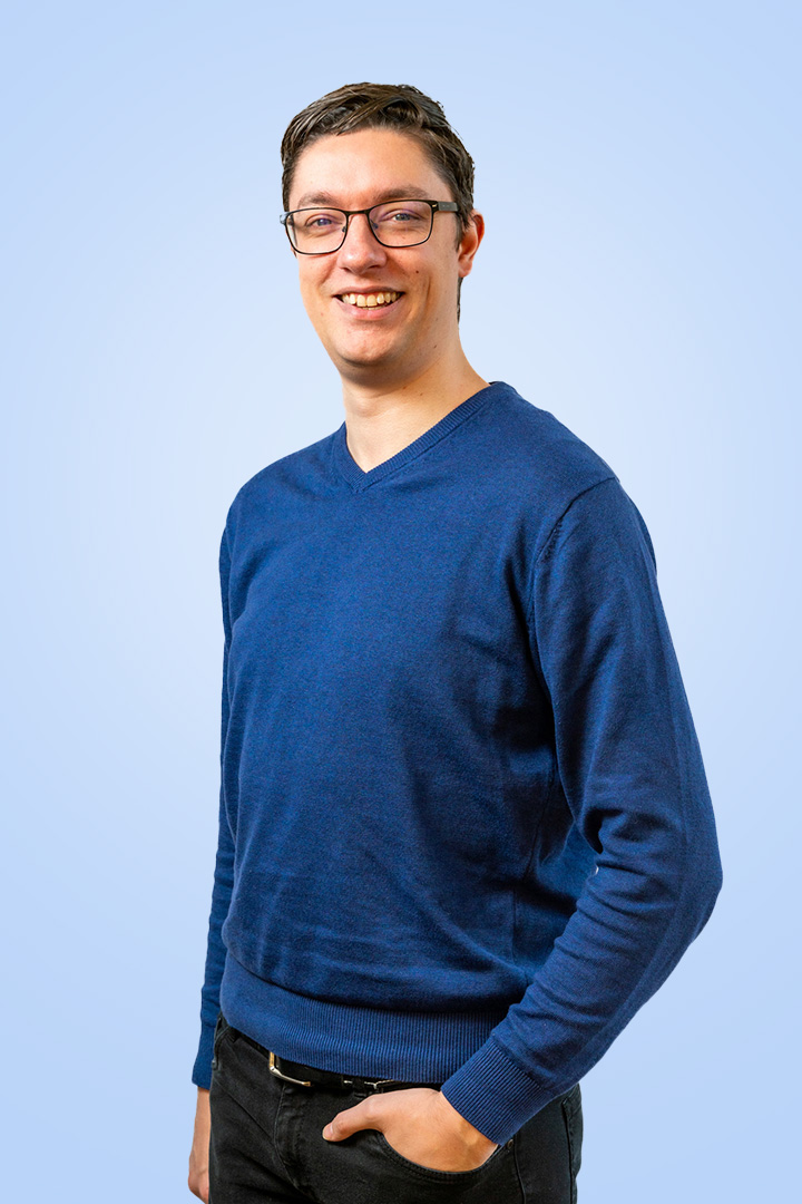 Man in blauwe trui met bril, lacht vriendelijk.
